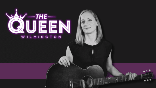 Liz Watkins holding a guitar stands confidently against a black background. "The Queen Wilmington" is written in bold purple and white text with a crown icon.